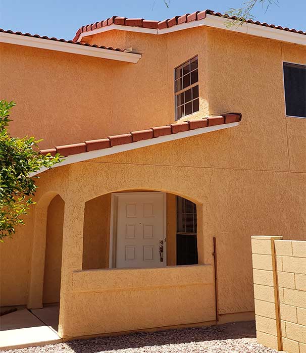 A tan house with red roof and white door.